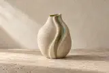 Vase de grès fictif Sillage, ivoire moucheté, relief plissé et glaçure vert sauge sur une surface en pierre.